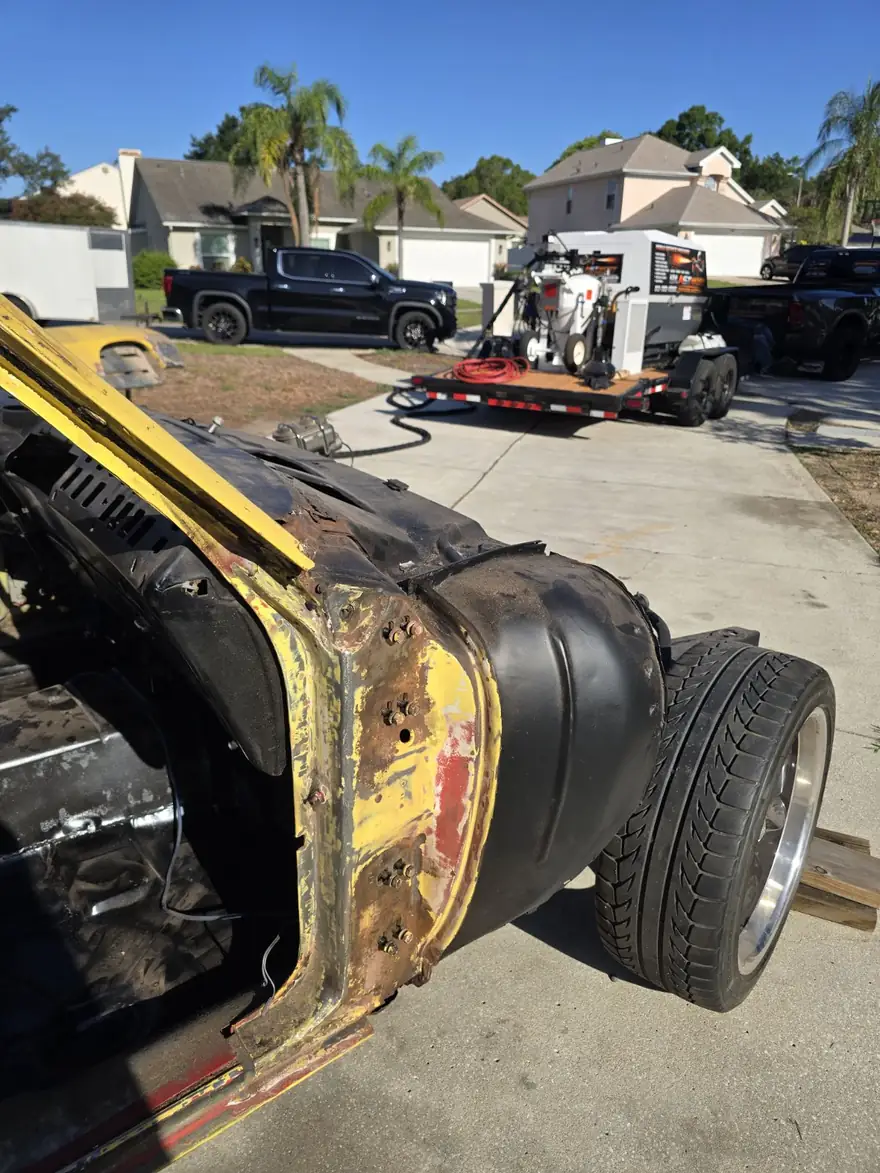 Front fender of a yellow project car with rust and old paint before blasting